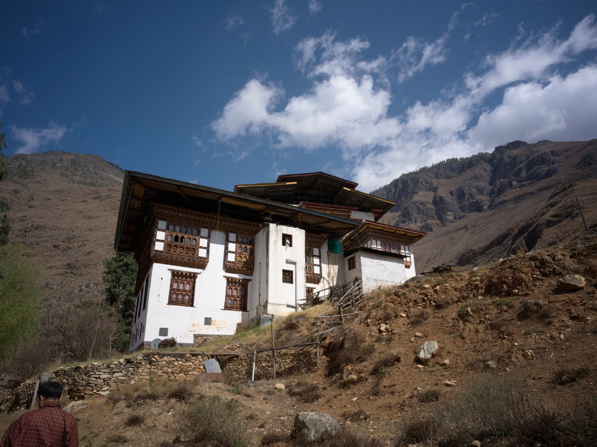 A traditional Bhutanese monastery building set against mountains and a bright sky