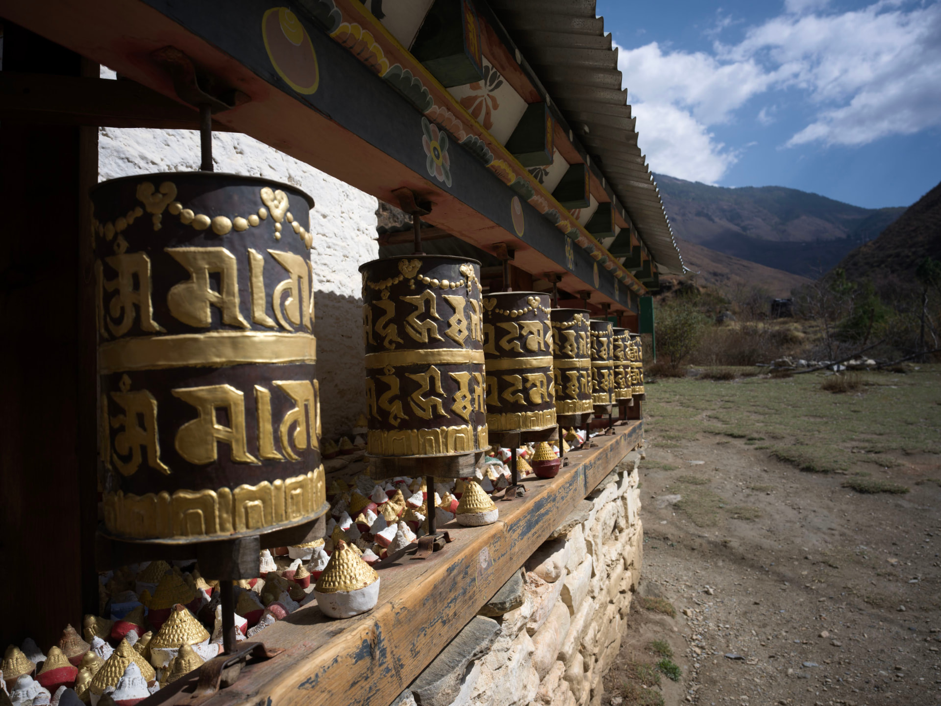 A row of ornate Bhutanese prayer wheels set against a mountain valley