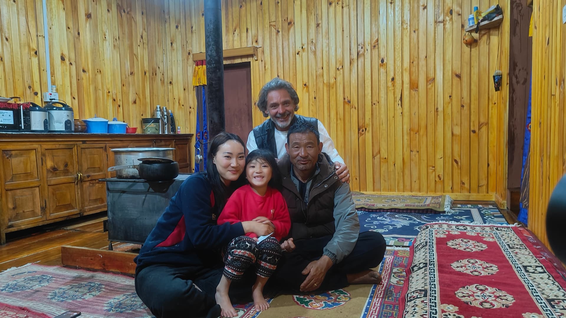 A Bhutanese family gathered inside a warmly lit traditional wooden farmhouse