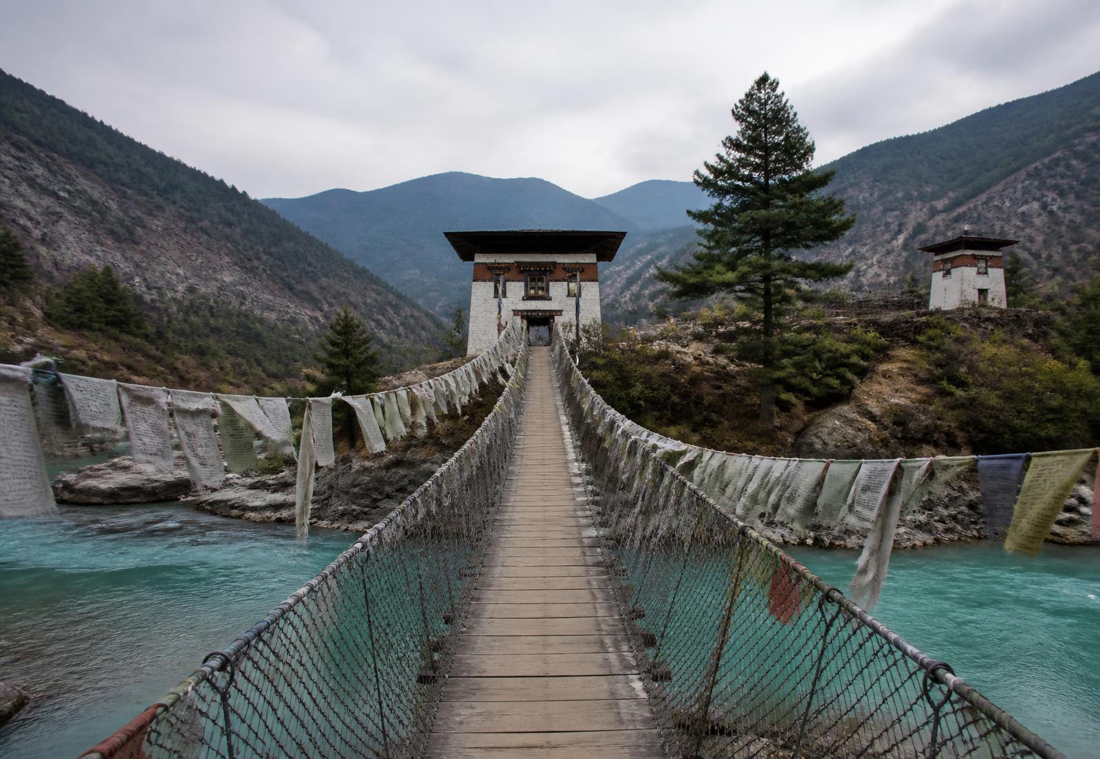 A footbridge hung with prayer flags crossing a Himalayan river in Bhutan